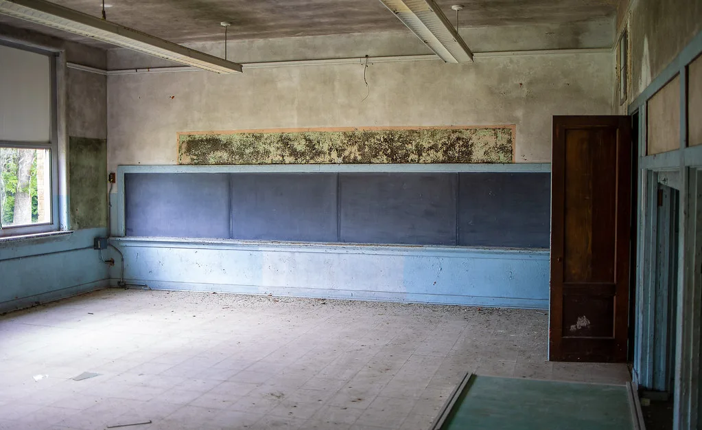 Empty old classroom with a long blackboard and deteriorated walls.