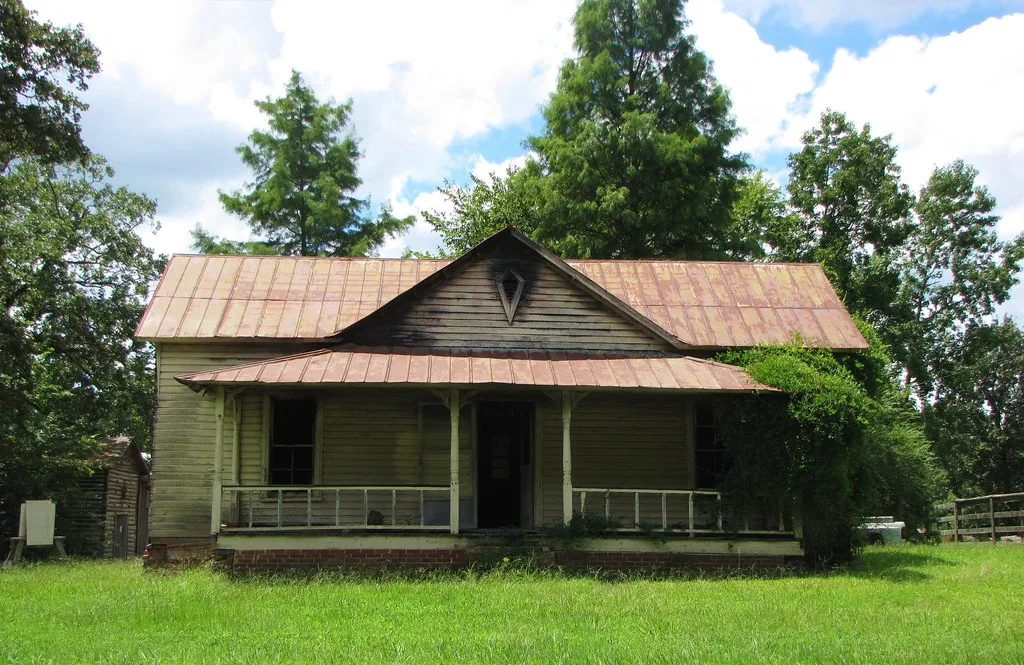 Old wooden house with a rusty roof and an overgrown porch.