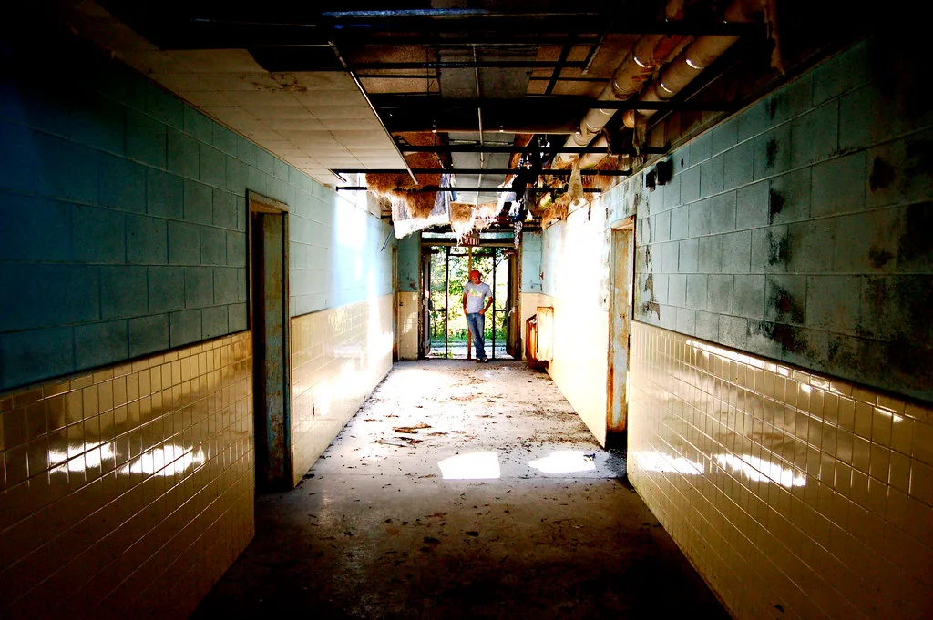 Derelict tiled corridor with a person at the far end.