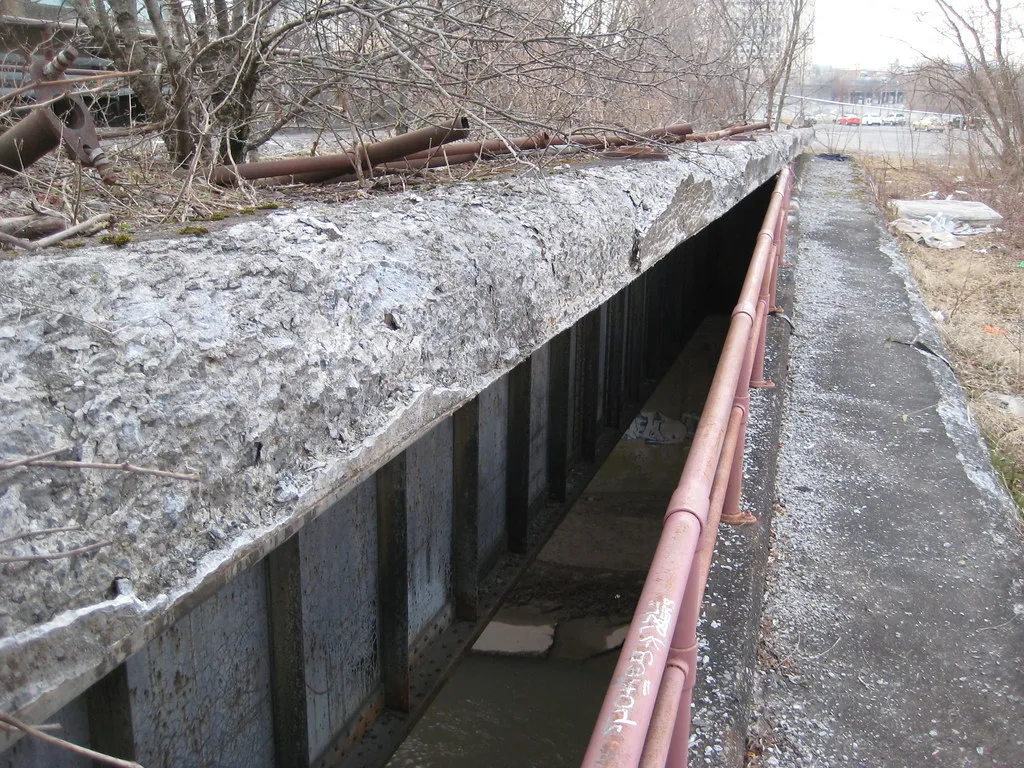 Old deteriorated covered concrete passage with a rusted railing.