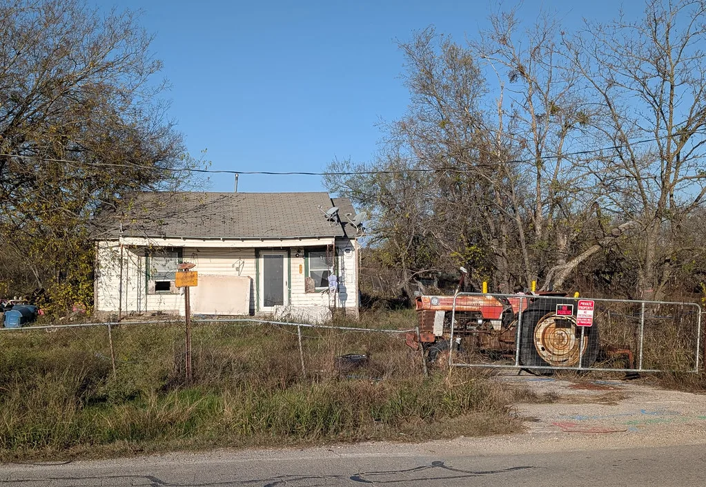 Petite maison dégradée et ancien tracteur derrière un grillage.