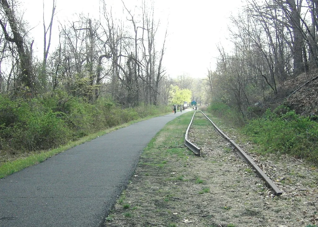 Disused railway track ending beside a tree-lined path.