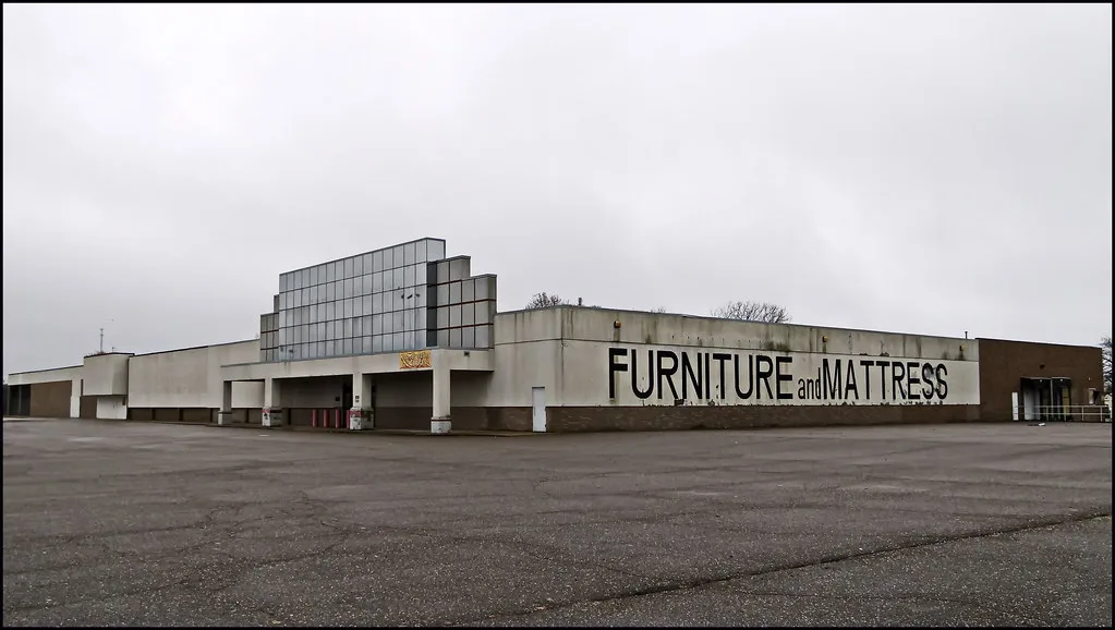 Ancien magasin de meubles avec façade basse et parking vide.