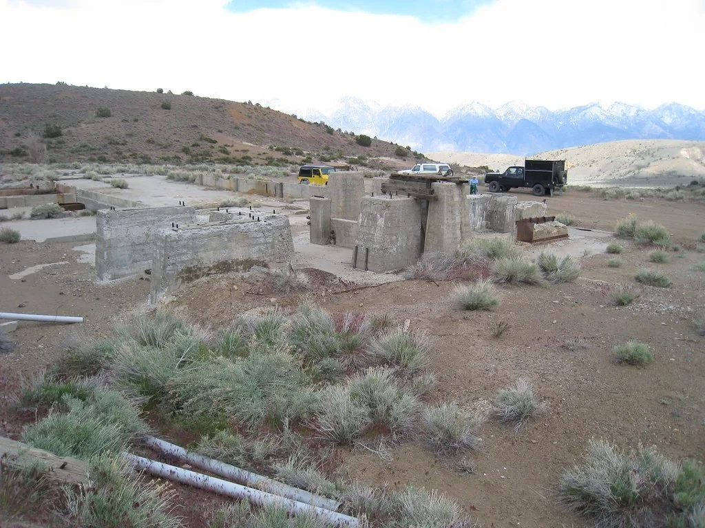 Remains of concrete industrial foundations with metal anchors on dry ground beneath mountains.