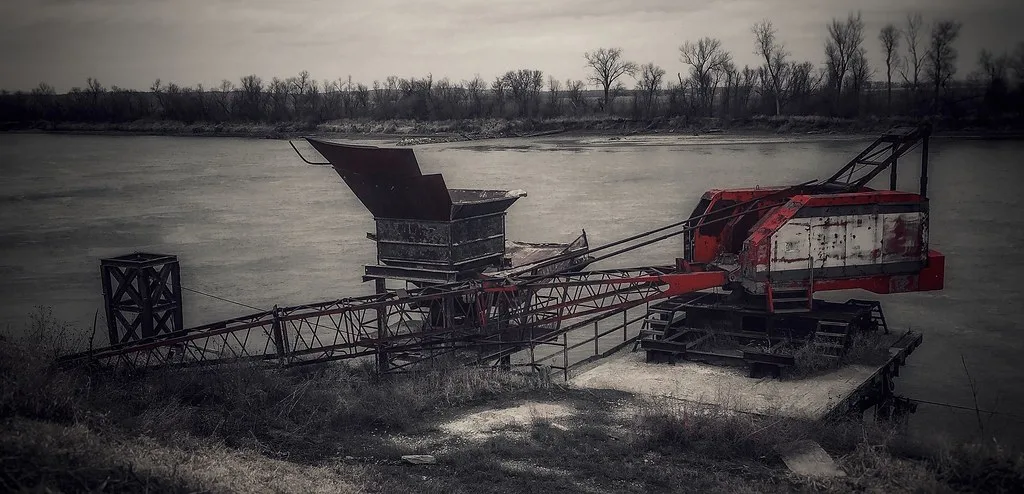 Old rusty crane and hopper beside a river.