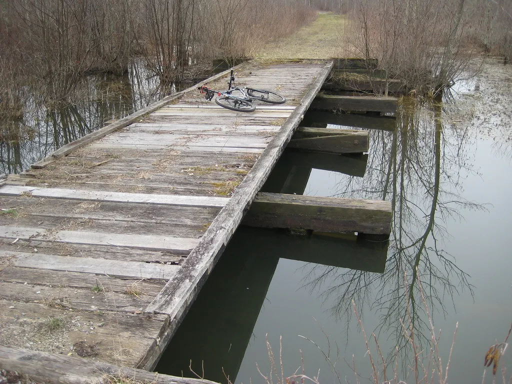 Deteriorated wooden bridge over water, with a bicycle on the remaining deck.
