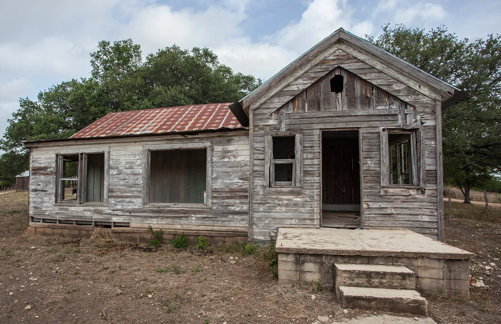 Ancienne maison en bois aux portes et fenêtres ouvertes.