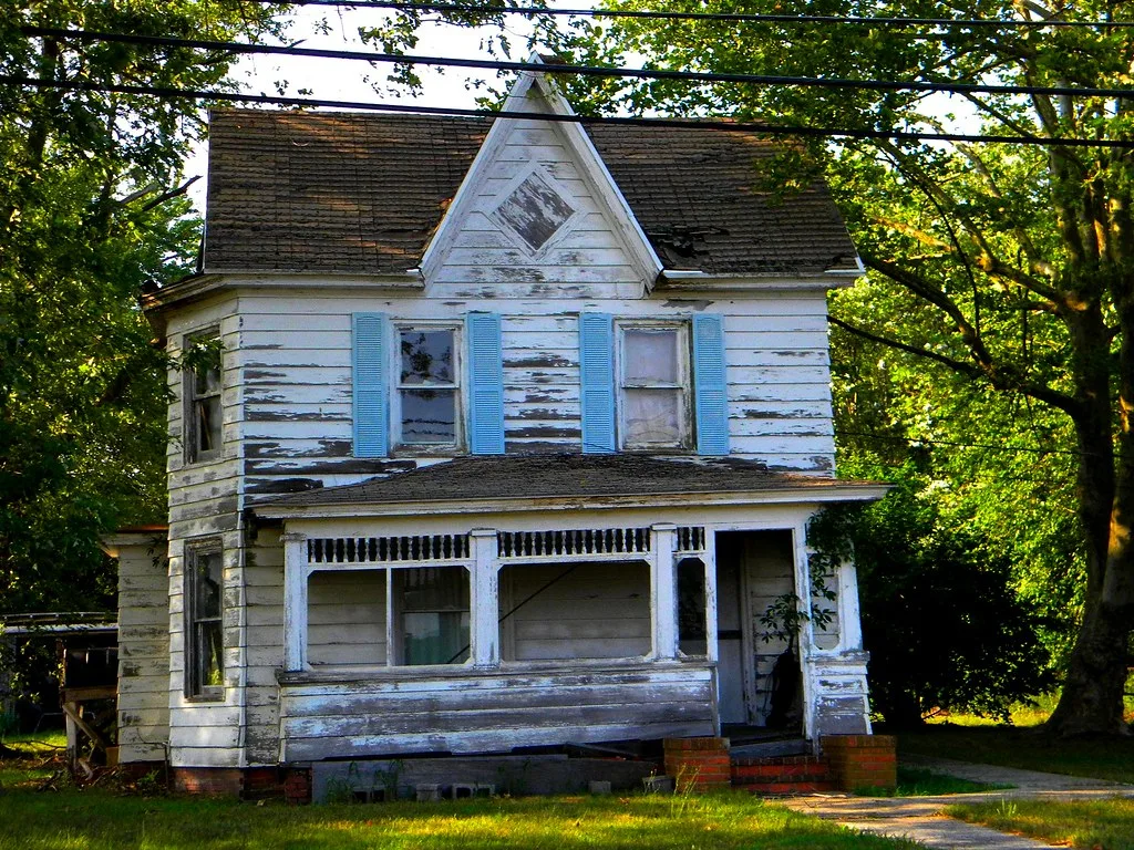 Old white house with a sagging porch and peeling paint.