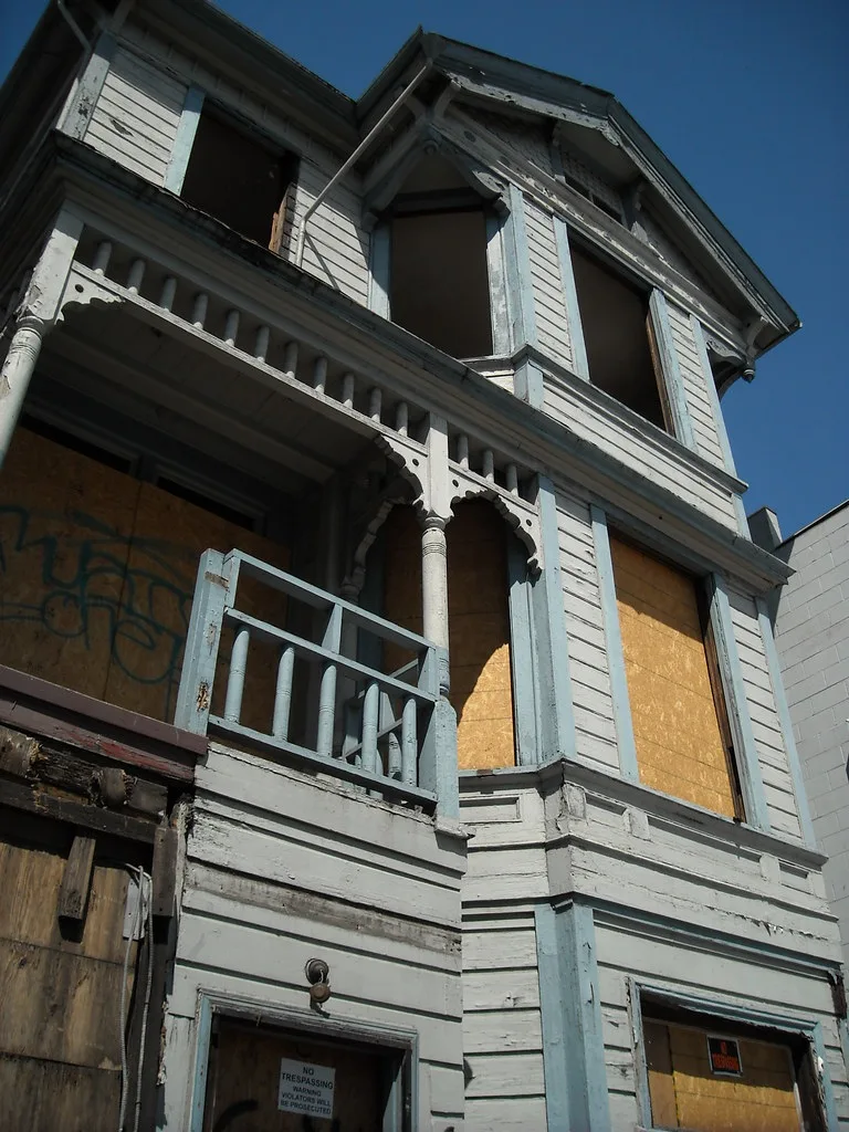 Ancienne maison de bois aux ouvertures condamnées et balcon dégradé.