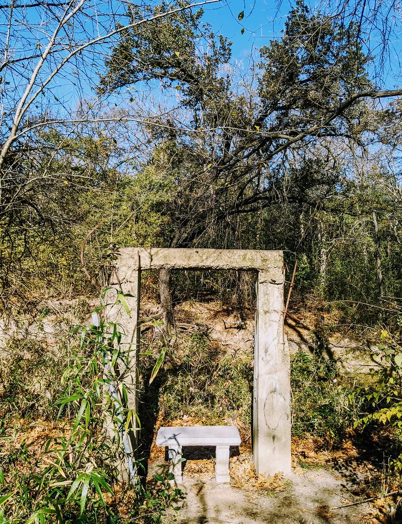 Encadrement de porte en béton au milieu de ruines envahies de végétation.