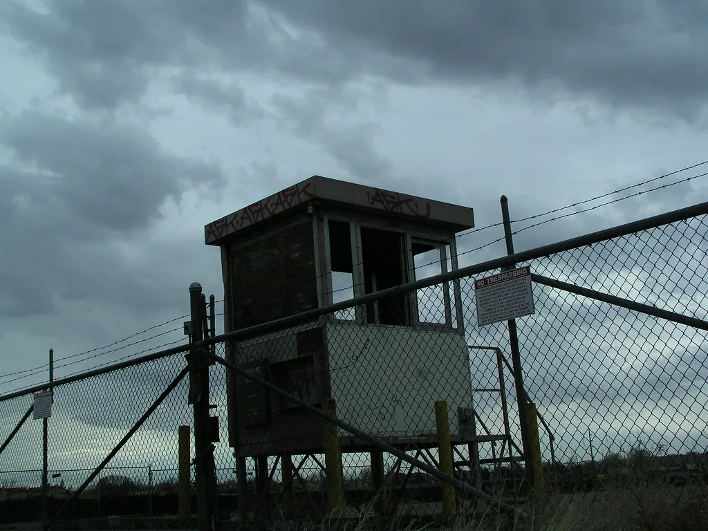 Old deteriorated elevated control booth behind a fence.
