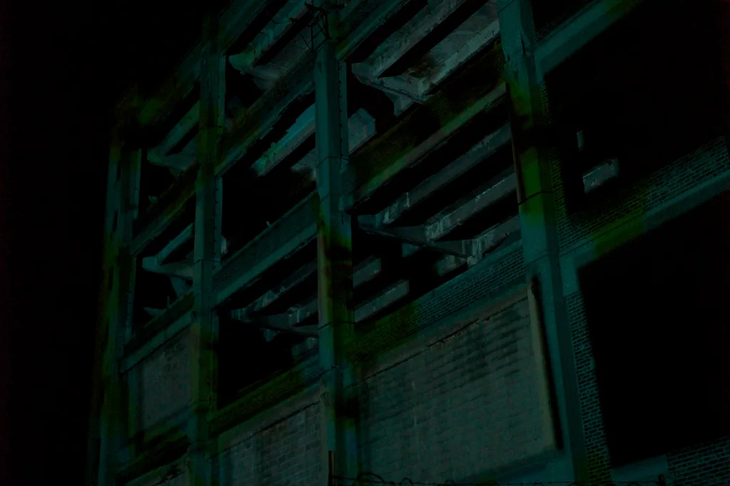 Gutted industrial facade with deteriorated concrete beams in the dark.