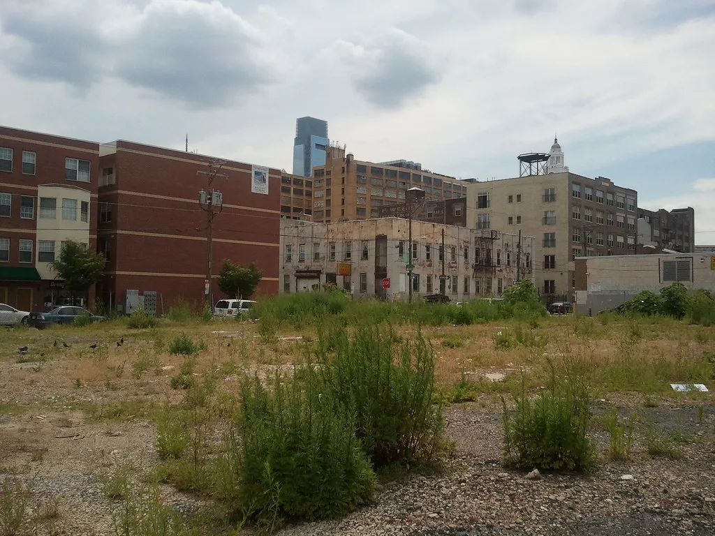 Deteriorated old building behind a weed-covered urban plot.