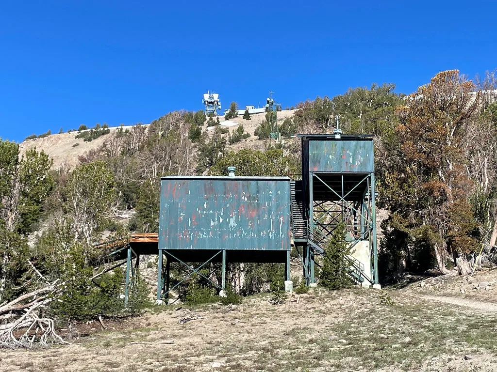 Anciennes installations métalliques sur pilotis dans une pente boisée.