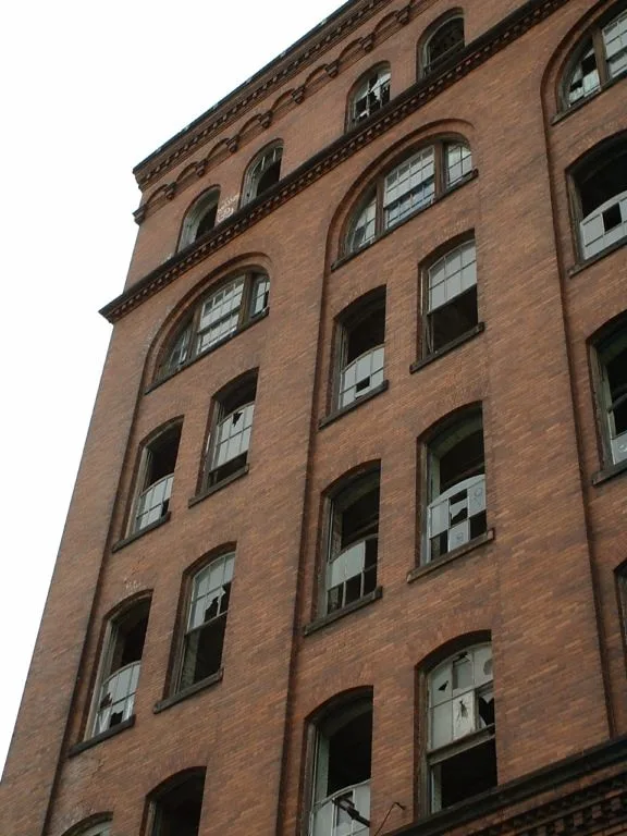 Tall brick facade with arched windows and numerous missing panes.