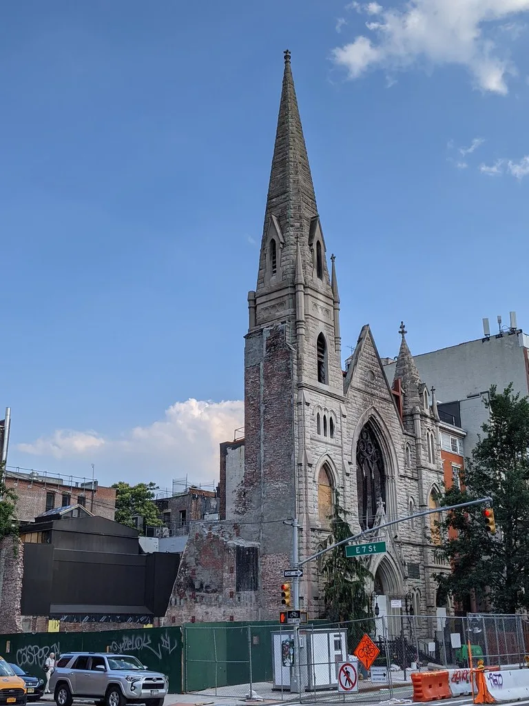 Façade et clocher d’une église en ruine aux baies obturées derrière des barrières de chantier.