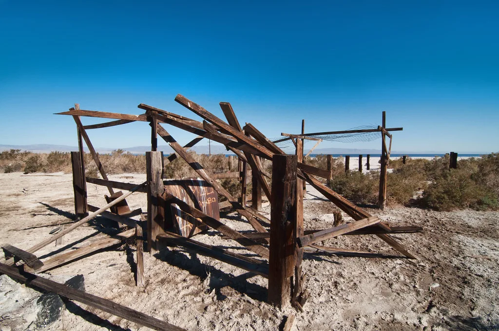 Collapsed wooden framework on sandy ground near water.
