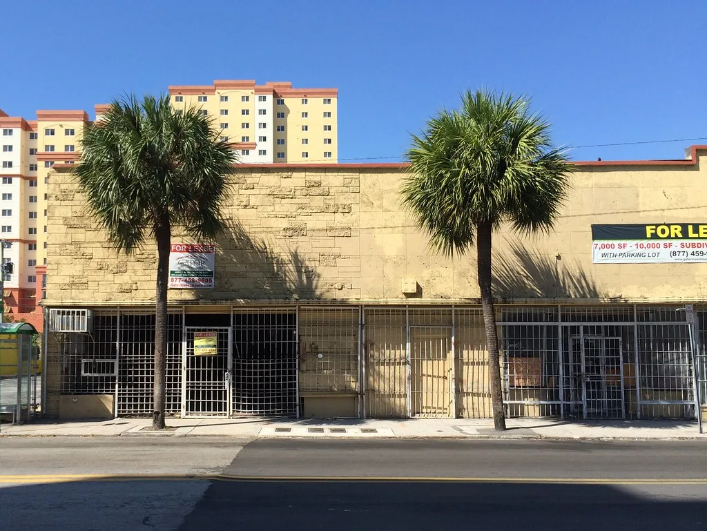 Façade commerciale vide fermée par des grilles sous deux palmiers.