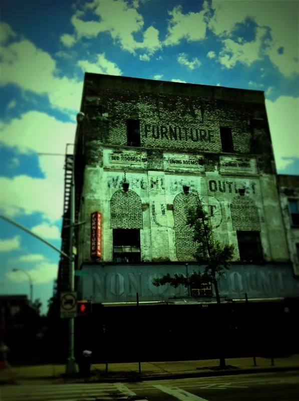 Old furniture shop with bricked-up windows, in green tones.