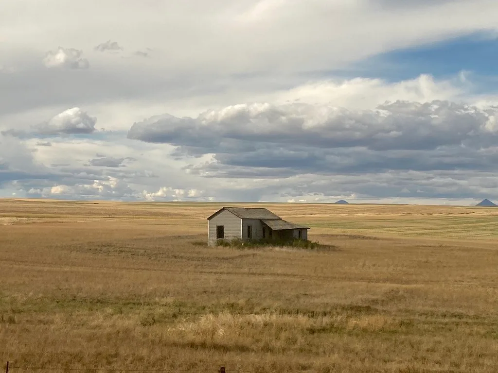 Old isolated house in a broad meadow under clouds.
