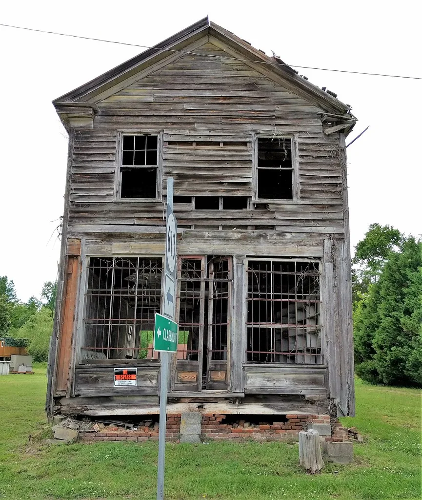 Bâtiment abandonné en bois à deux niveaux, aux vitrines brisées et aux fondations affaissées.