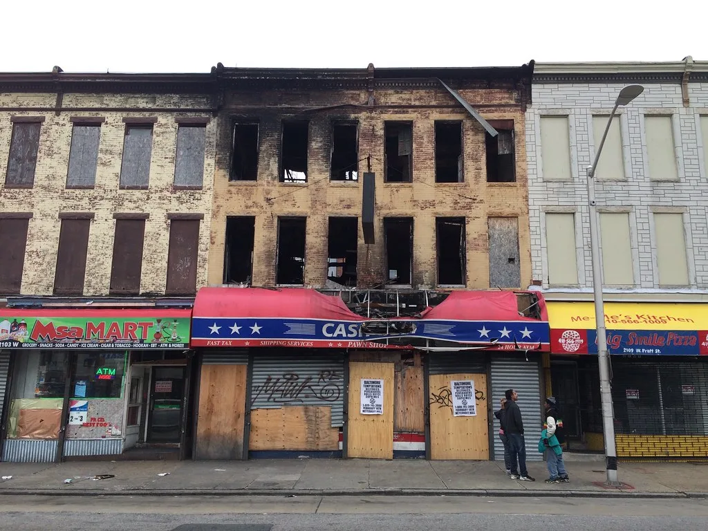 Brick building with empty, blackened windows above a boarded shop.