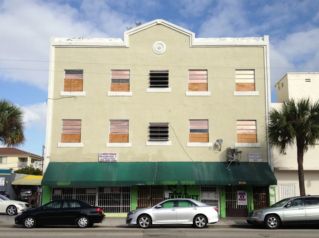 Pale building with boarded windows above a former shop with a green awning.