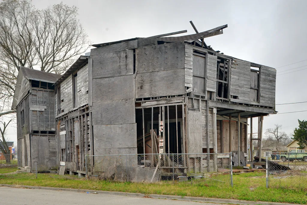 Ancien bâtiment de bois éventré derrière un grillage.