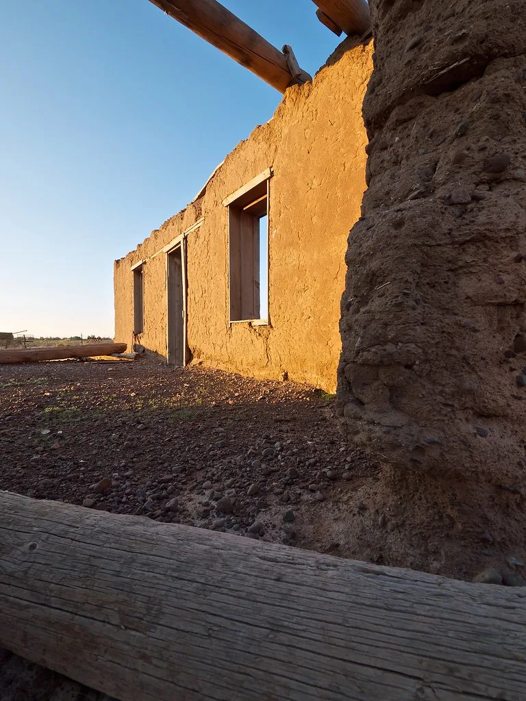 Mur d’adobe d’un bâtiment en ruine sans toit, éclairé par le soleil bas.