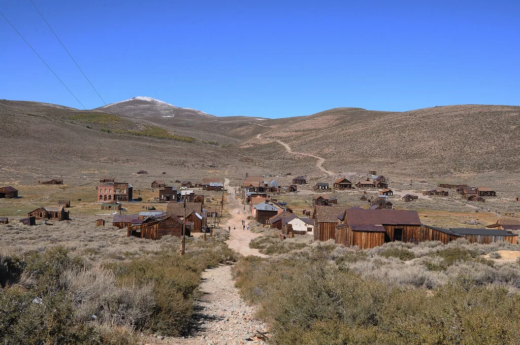 Old village of neglected wooden houses at the foot of arid hills, crossed by a dirt track.