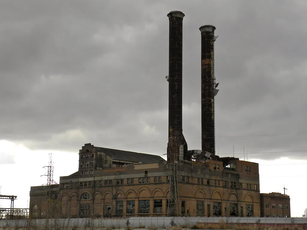 Old factory with broken windows beneath two tall chimneys.
