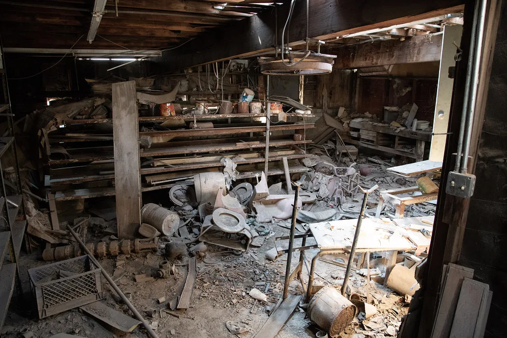 Ancien atelier encombré d’outils et de débris sous une toiture dégradée.