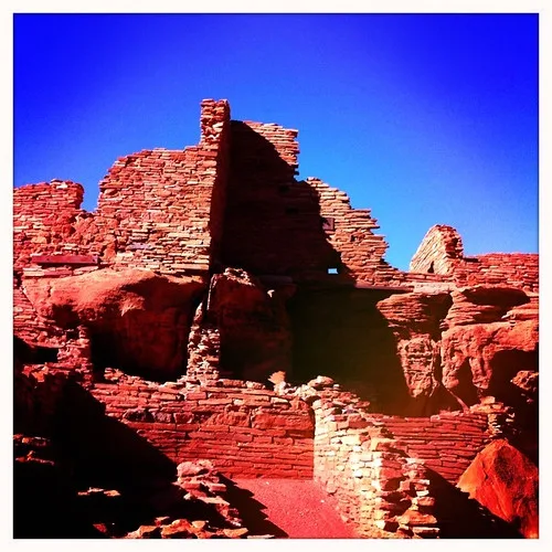 Ruins of roofless, partially collapsed red stone walls on rocky terrain beneath a deep blue sky.