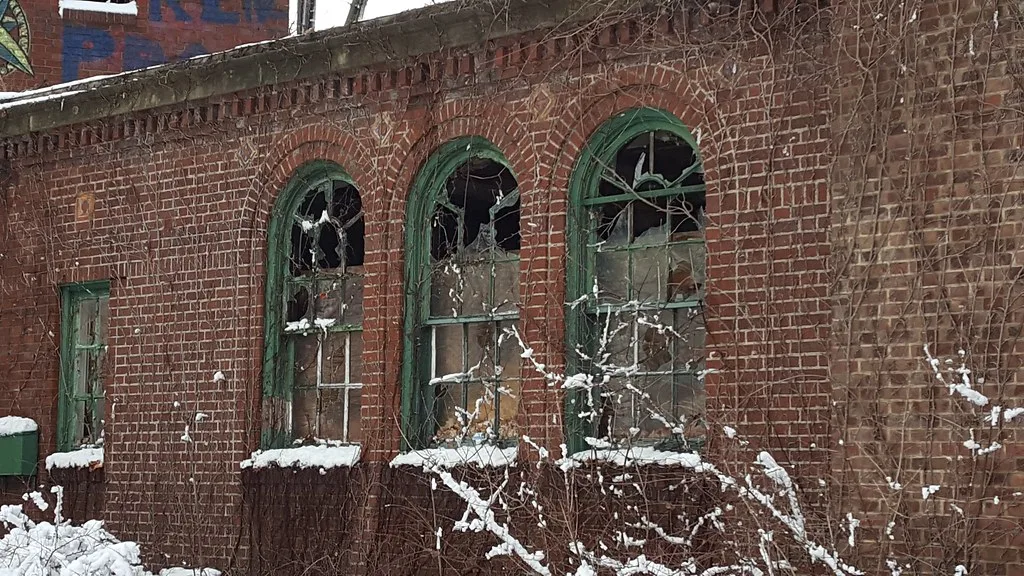 Three broken green arched windows on an abandoned brick building in snow.