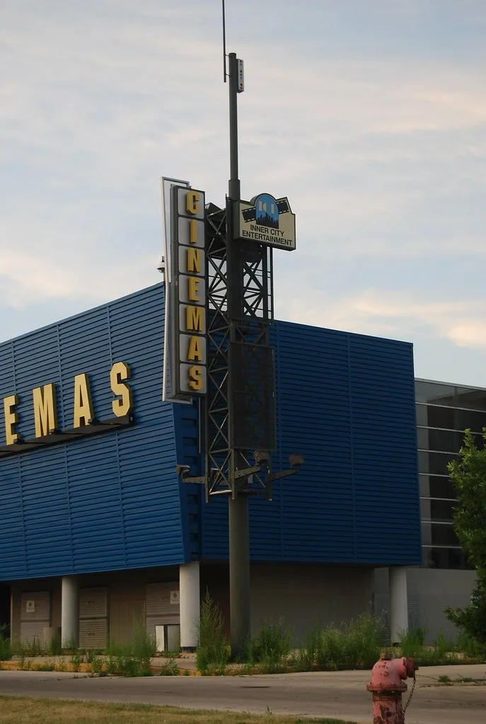 Façade bleue d’un cinéma désaffecté aux portes condamnées, bordée de hautes herbes.