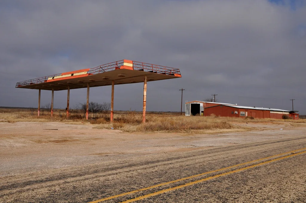 Old fuel station without pumps and a low building in tall grass.