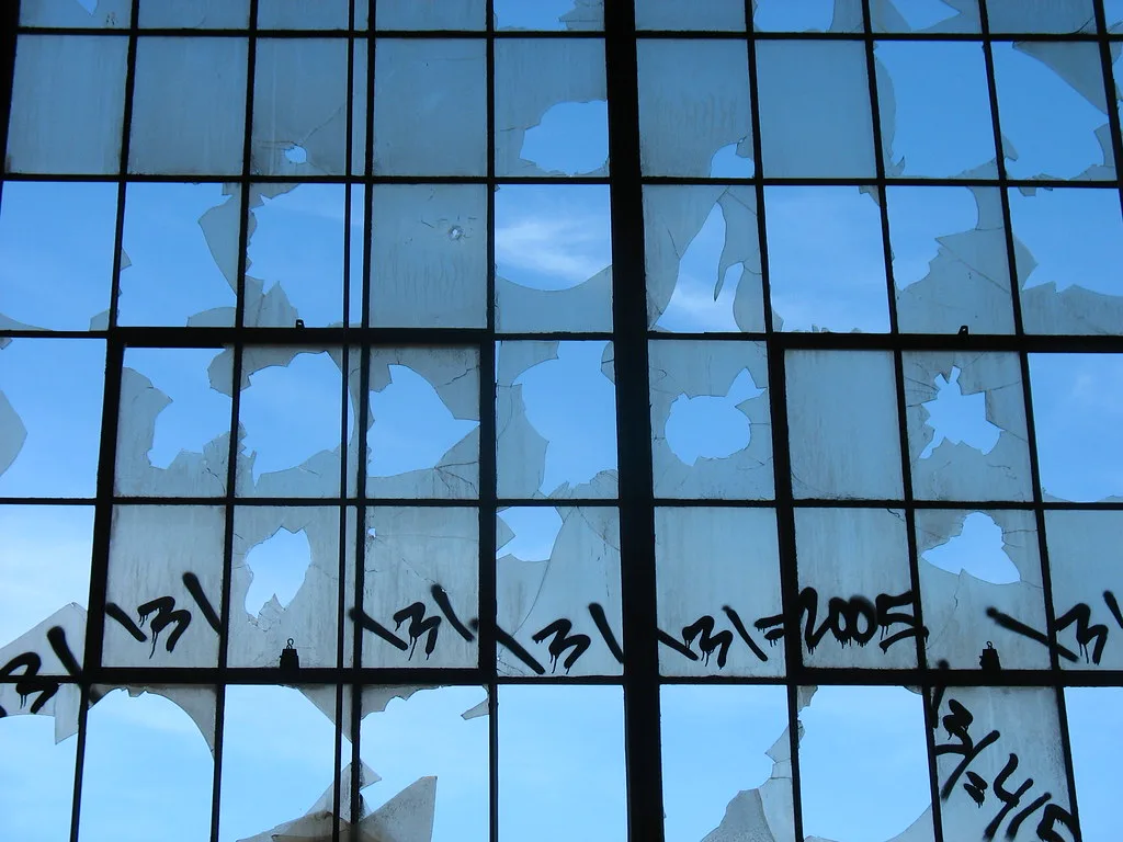 Broken window grid with graffiti revealing the blue sky.