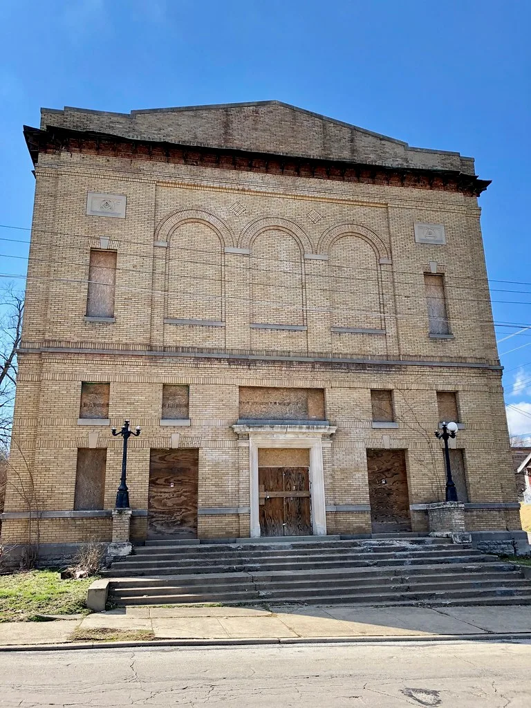 Large abandoned yellow-brick building with boarded openings above a wide cracked staircase.