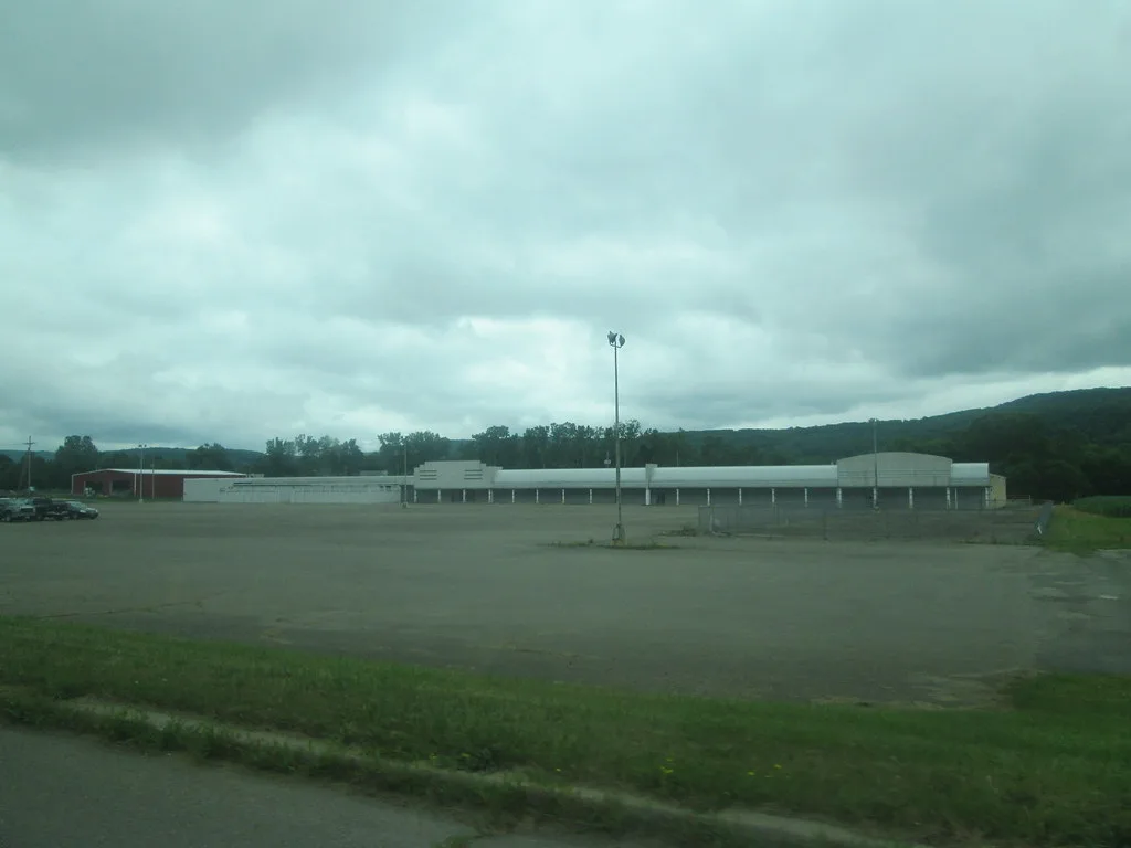 Closed old shopping complex behind a deteriorated parking lot.