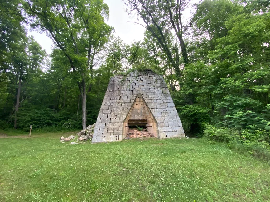 Partly ruined old stone furnace in a grassy clearing.