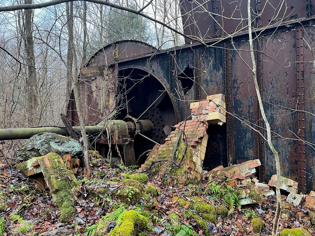 Machinerie industrielle rouillée parmi des briques effondrées dans les bois.
