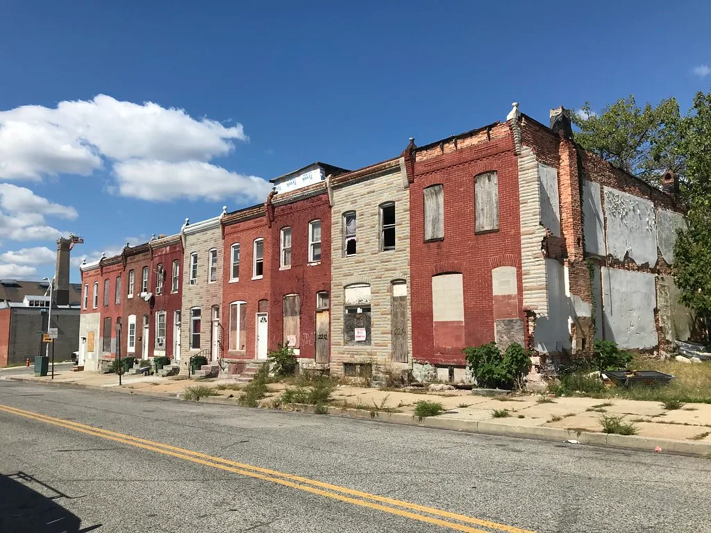 Row of brick houses with boarded openings and deteriorated walls.