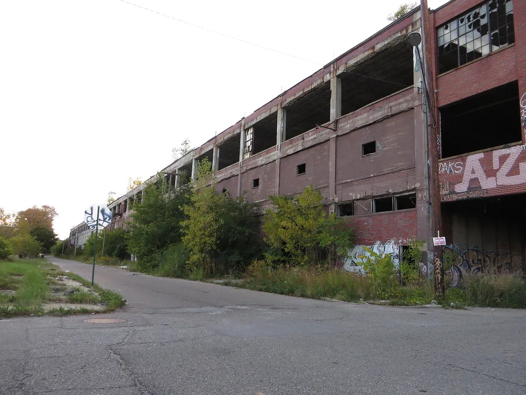 Long bâtiment industriel en ruine au bord d’une chaussée dégradée.