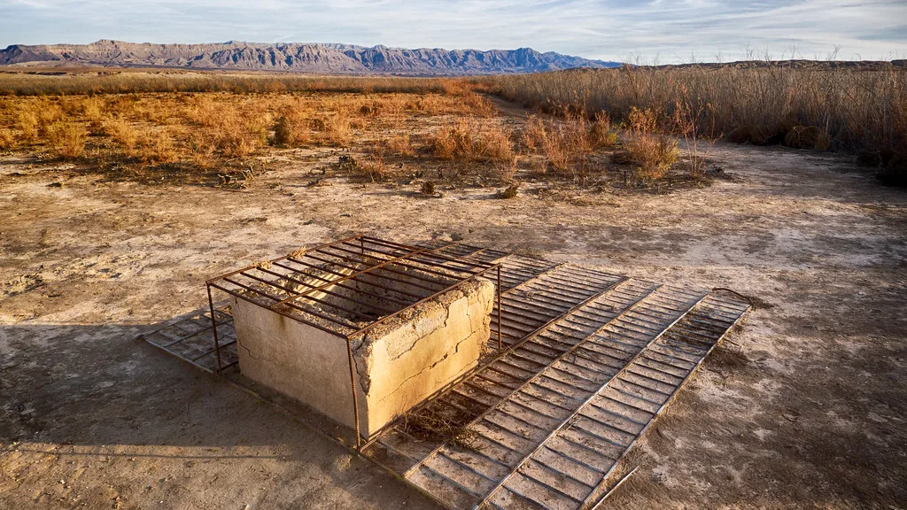 Old masonry cistern with rusty grates on dry ground.