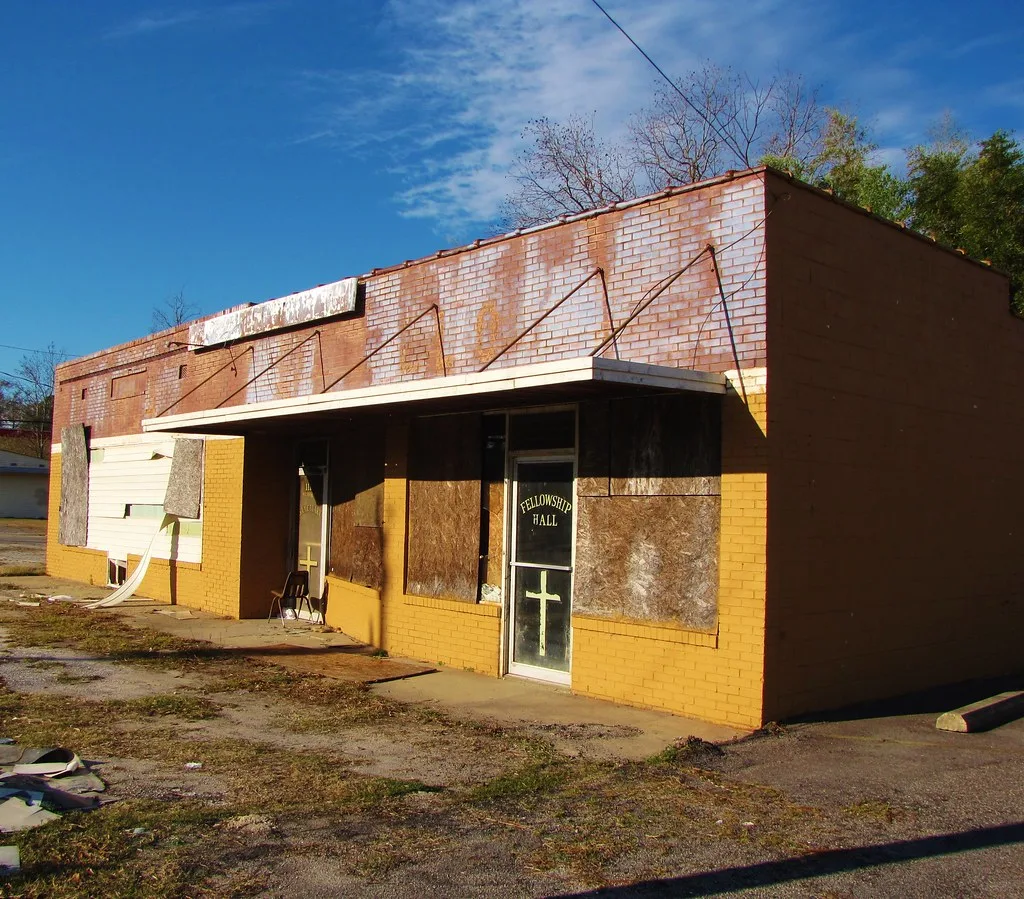 Old yellow premises with boarded windows and torn cladding around the doors.