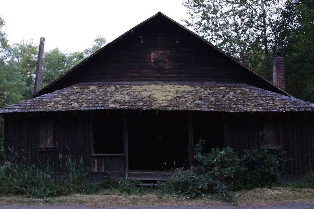 Maison abandonnée en bois aux fenêtres condamnées sous une toiture couverte de mousse.