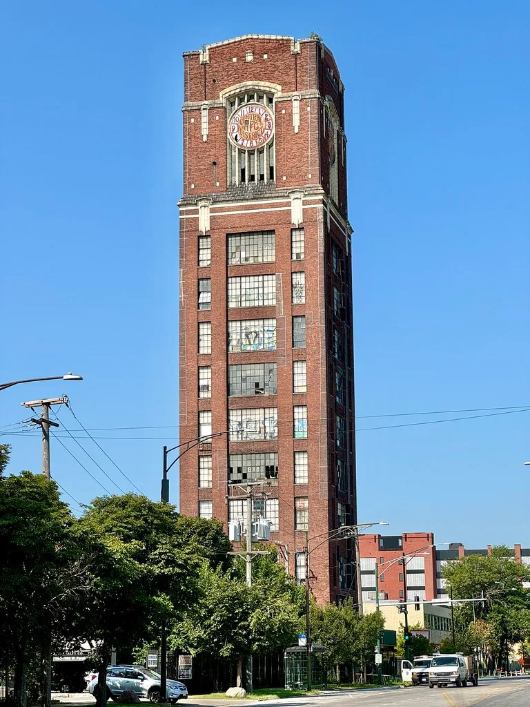 Haute tour industrielle de briques avec horloge et fenêtres brisées.