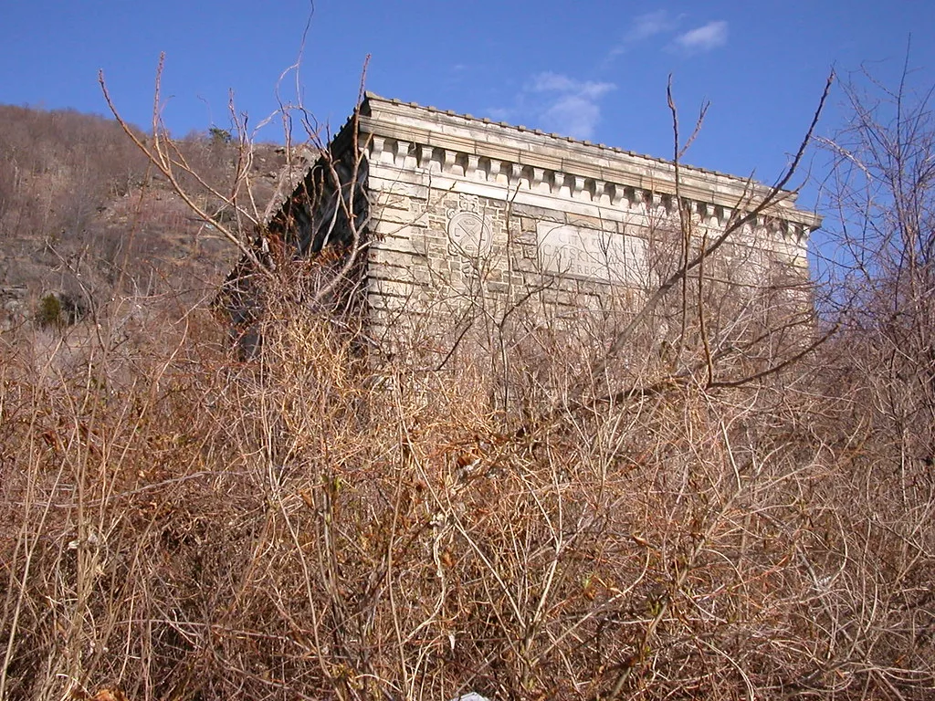 Ancien ouvrage de pierre orné de reliefs au milieu des broussailles.