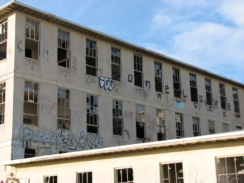 Facade of an old hospital with many broken windows and graffiti-covered walls.