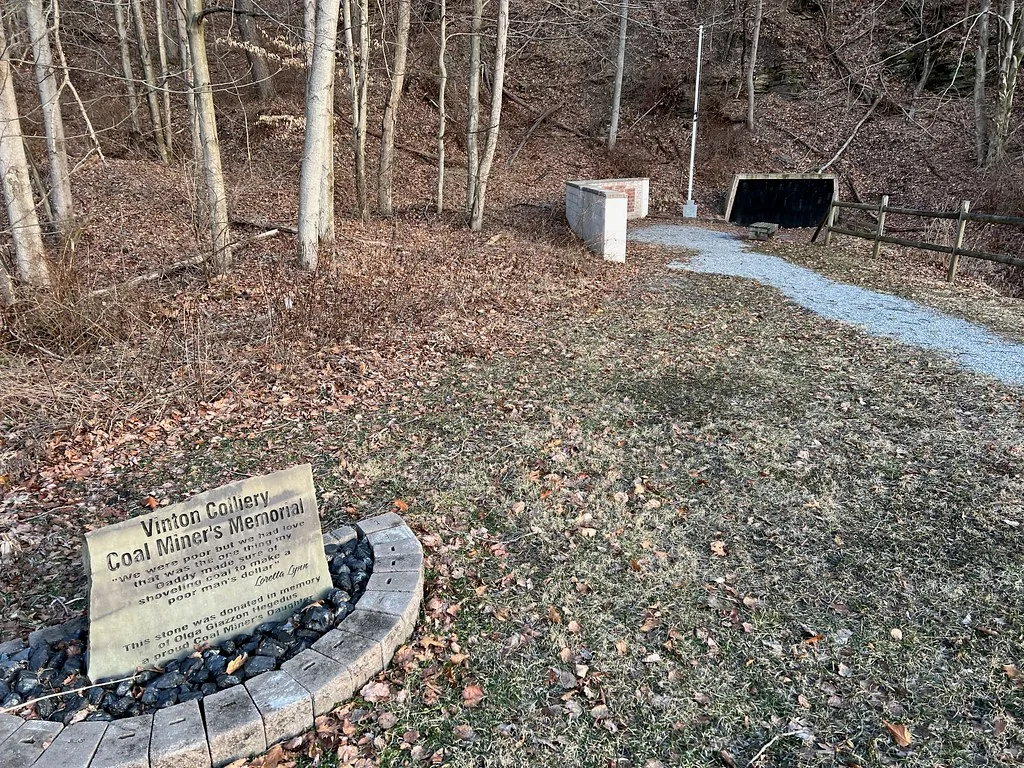 Ancienne entrée de mine fermée et mémorial des mineurs dans un sous-bois.